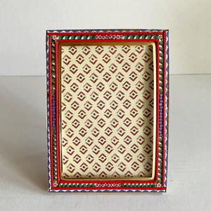 May include: Rectangular photo frame with a patterned interior and a decorative border. The frame has a red, blue, green, and gold border. The interior pattern is a repeating diamond design in red on a cream background.