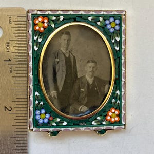 May include: A rectangular picture frame with a central oval opening containing a black and white photograph of two individuals. The frame is decorated with a mosaic of green, orange, blue, and white tiles. A ruler shows the frame is 2 inches tall.