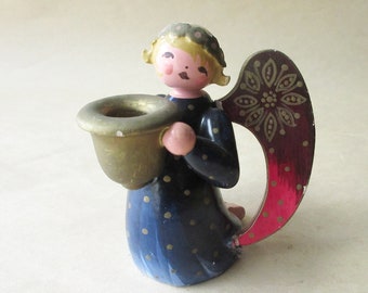 Op de afbeelding: Een houten engelenbeeldje met een beker in messingkleur. De engel draagt een blauwe jurk met gouden stippen en heeft blond haar. De vleugels zijn rood met een gouden bloemmotief. Het beeldje is een decoratief item.