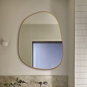 May include: A modern bathroom vanity with a white porcelain sink, a light brown countertop, and a large, organic-shaped mirror with a wooden frame. The mirror is reflecting a light purple wall.