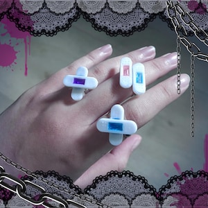 May include: Three white plastic rings shaped like bandages with colorful accents. The rings have a blue, pink, and purple accent.