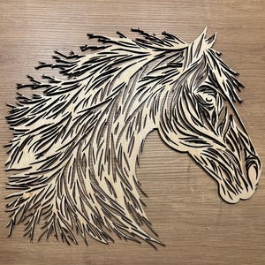 Puede incluir: Un recorte de madera de la cabeza de un caballo con un diseño detallado e intrincado. La crin y la cara del caballo están formadas por muchas líneas y curvas pequeñas, creando un aspecto texturizado.