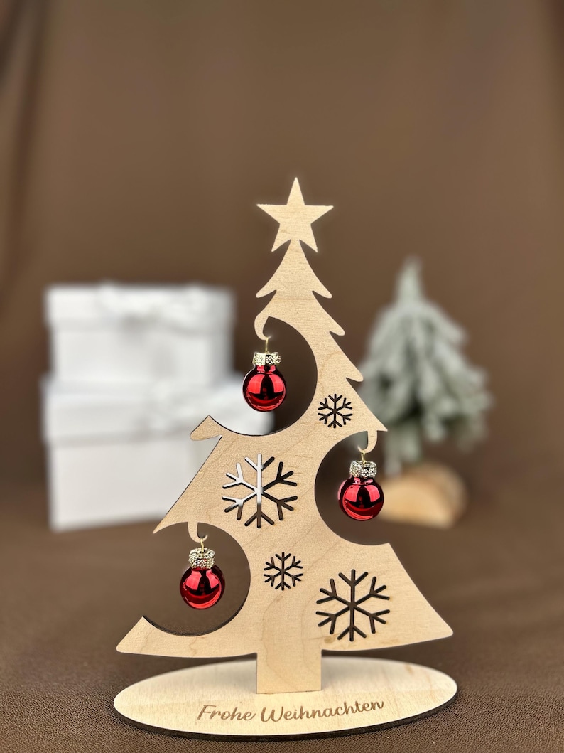 May include: Wooden Christmas tree decoration with red ornaments and snowflake cutouts. The tree has a star on top and the words "Frohe Weihnachten" on the base. A festive holiday decoration.
