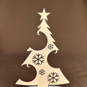 May include: A wooden Christmas tree decoration with a star on top and snowflake cutouts. The base reads "Frohe Weihnachten". The tree is made of light-colored wood and stands on a round base.