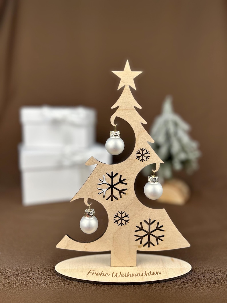 May include: A wooden Christmas tree decoration with a star on top and snowflake cutouts. It features three small, silver-colored ornaments. The base reads "Frohe Weihnachten".