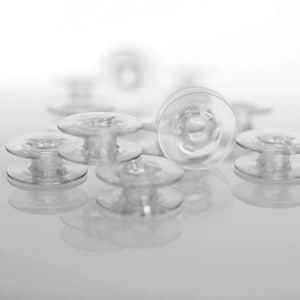 Peut inclure: Un groupe de canettes en plastique transparent pour une machine à coudre. Les canettes sont disposées de manière aléatoire sur une surface blanche.