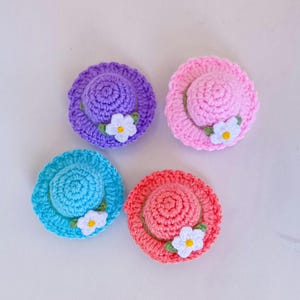 Puede incluir: Cuatro sombreros de ganchillo con adornos florales. Los sombreros son en tonos de rosa, morado, azul y coral.