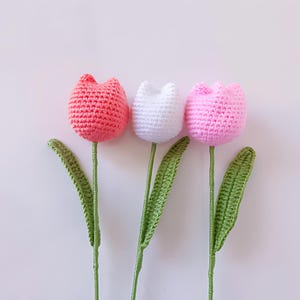 Op de afbeelding: Drie gehaakte tulpen in roze, wit en koraal met groene stelen en bladeren.