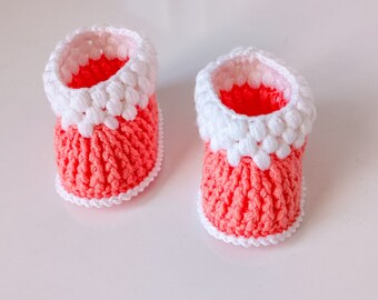 Op de afbeelding: Een paar roze en witte gehaakte babyschoentjes. De schoentjes hebben een witte gehaakte rand rond de bovenkant en een roze gehaakte zool.