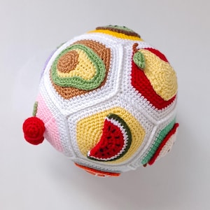 Puede incluir: Una bola de crochet con forma de fruta, con diferentes secciones de colores que representan sandía, aguacate, pera y otras frutas.