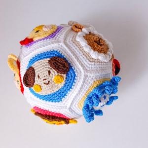 Peut inclure: Un jouet en forme de balle crocheté multicolore avec différents visages d'animaux sur chaque face. La balle est faite de fil blanc avec des accents de différentes couleurs. Les visages d'animaux comprennent un chien, un chat, un oiseau et un poisson.