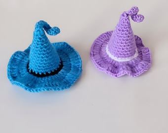 May include: Two crocheted witch hats, one blue and one purple. The blue hat has a black brim and a pointed top. The purple hat has a white trim and a pointed top.