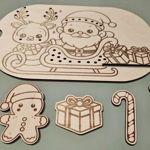 Op de afbeelding: Houten kerstthema-uitsparingen. De kerstman en een rendier in een slee staan ​​op een groot ovaal stuk. Extra uitsparingen zijn cadeaudozen, een peperkoeken man, een zuurstok en een teddybeer.