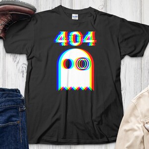 May include: Black t-shirt featuring a white ghost graphic with red, blue, and yellow 3D effect. The text "404" is above the ghost. The shirt is displayed with blue jeans, a brown boot, a tan jacket, and glasses.