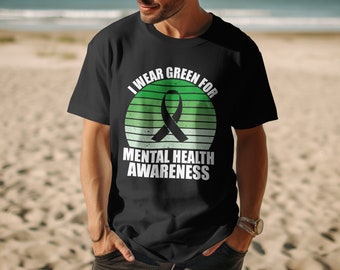 May include: A black t-shirt with a green and white retro sunset graphic. The graphic features a black ribbon and the text "I wear green for mental health awareness".