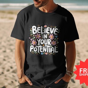 Könnte beinhalten: Schwarzes T-Shirt mit floralem Design und dem Text "Glaube an dein Potenzial".