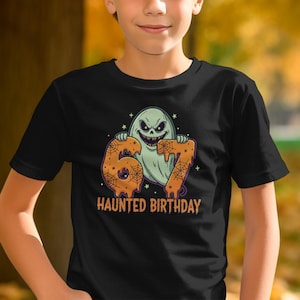 Może przedstawiać: Czarny t-shirt z motywem Halloween. Projekt przedstawia zielonego ducha trzymającego liczby "67" w upiornej czcionce, z napisem "HAUNTED BIRTHDAY" poniżej. Koszulka jest noszona przez dziecko.