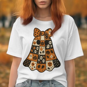 Peut inclure: T-shirt blanc avec un motif de fantôme d'Halloween. Le fantôme est fait de patchwork avec un nœud, et comprend des citrouilles, des crânes et des feuilles aux couleurs orange, noir et crème. Le motif est centré sur le t-shirt.