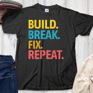 May include: Black t-shirt with the text "BUILD. BREAK. FIX. REPEAT." in colorful letters.
