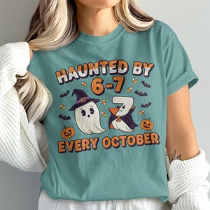 Może przedstawiać: Turkusowa koszulka z napisem "HAUNTED BY 6-7 EVERY OCTOBER". Koszulka zawiera grafikę o tematyce Halloween, w tym ducha w kapeluszu czarownicy, wampira, nietoperze, dynie i cukierki.