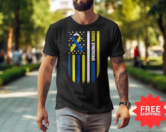 Può includere: Maglietta nera con un design a nastro blu e giallo su sfondo bianco. Il nastro è un simbolo della consapevolezza della sindrome di Down. Il testo "Down Syndrome Awareness" è scritto verticalmente sul lato destro del nastro.