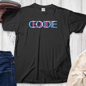 Puede incluir: Camiseta negra con la palabra "CODE" en letras de bloque azules, rosas y blancas. La camiseta se muestra con un par de botas marrones, vaqueros azules y una chaqueta beige con gafas.