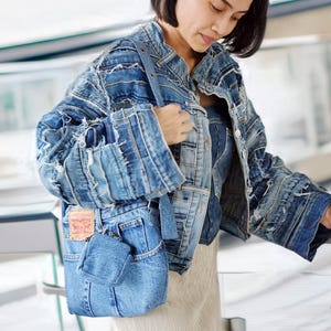 Può includere: Una giacca di jeans blu con un design patchwork e una borsa tote di jeans blu con un'etichetta rossa e bianca. La giacca è realizzata con più strati di tessuto di jeans e ha un bordo sfrangiato. La borsa tote è realizzata con un solo strato di tessuto di jeans e ha una chiusura a zip.