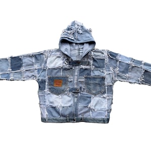 Puede incluir: Una chaqueta vaquera azul con un diseño de patchwork y capucha. La chaqueta tiene un aspecto desgastado con bordes deshilachados y costuras.