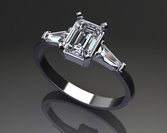 May include: A silver engagement ring with a large emerald-cut diamond center stone and two smaller baguette diamonds on either side. The ring has a sleek, modern design with a polished finish, reflecting light. The ring is set on a dark background.
