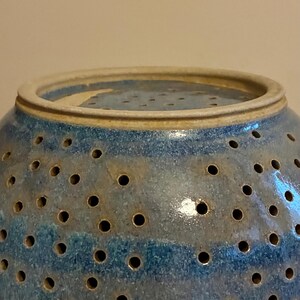 K&ouml;nnte beinhalten: Eine blaue Keramik-Dekoschale mit zahlreichen kleinen L&ouml;chern. Die Schale hat eine runde Form mit einem leicht ausgestellten Rand. Die Farbe ist eine Mischung aus Blau und Beige, mit gl&auml;nzendem Finish. Die Schale ist wahrscheinlich handgefertigt.