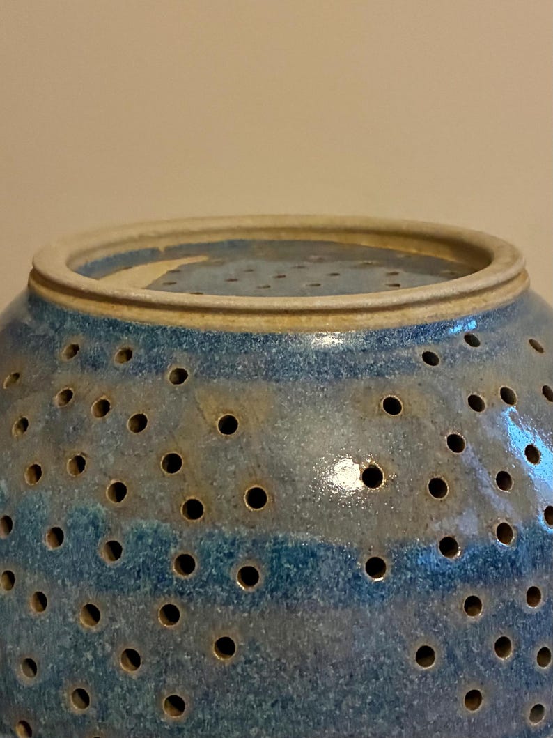 K&ouml;nnte beinhalten: Eine blaue Keramik-Dekoschale mit zahlreichen kleinen L&ouml;chern. Die Schale hat eine runde Form mit einem leicht ausgestellten Rand. Die Farbe ist eine Mischung aus Blau und Beige, mit gl&auml;nzendem Finish. Die Schale ist wahrscheinlich handgefertigt.