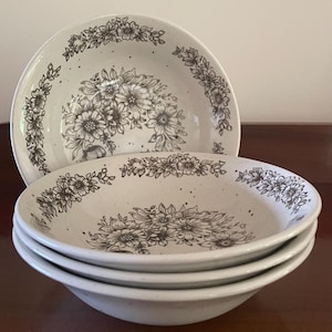 May include: Set of four white ceramic bowls with a brown floral pattern. The bowls have a speckled glaze and a slightly rounded shape.