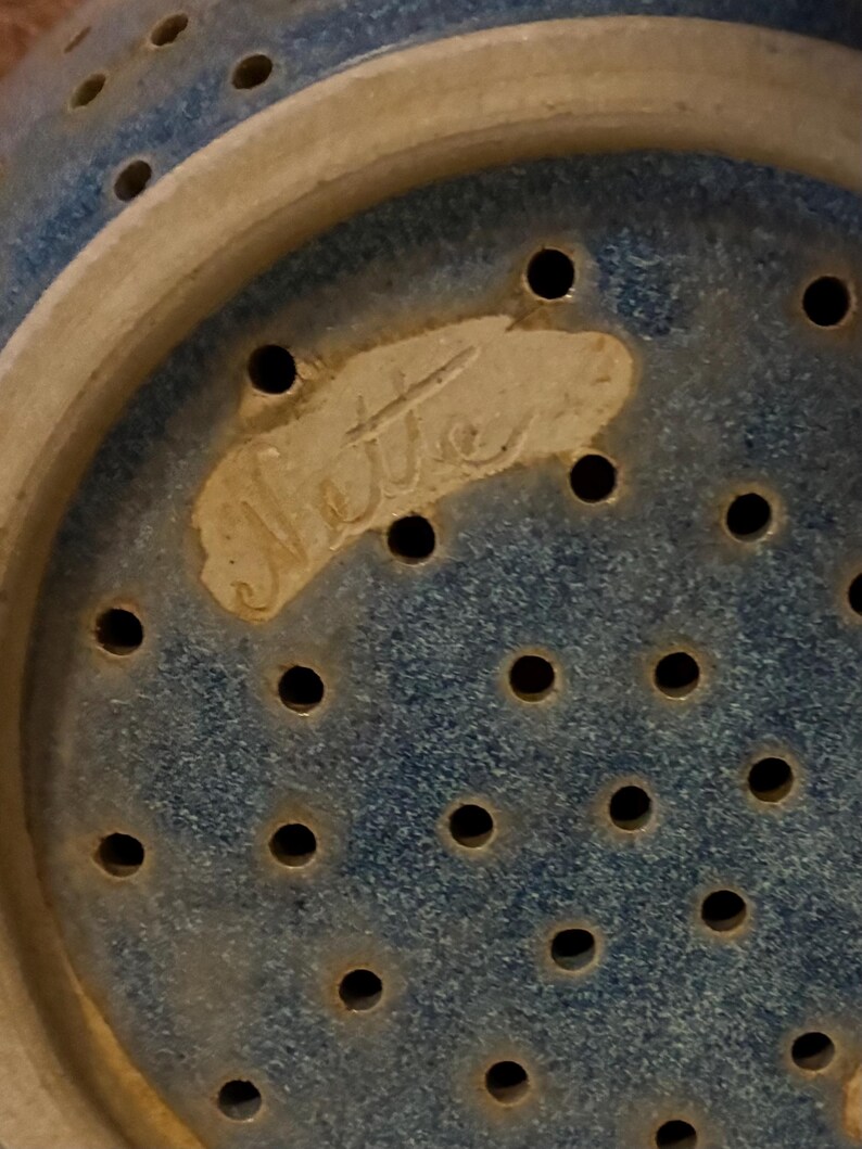 K&ouml;nnte beinhalten: Nahaufnahme einer blauen Keramik-Gem&uuml;sesch&uuml;ssel mit zahlreichen kleinen L&ouml;chern. Die Gem&uuml;sesch&uuml;ssel hat einen hellfarbigen Rand und eine strukturierte Oberfl&auml;che. Das Wort "Nette" ist unten eingeschrieben.