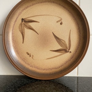 May include: A brown ceramic plate with a light brown glaze and a design of stylised leaves in a darker brown colour.