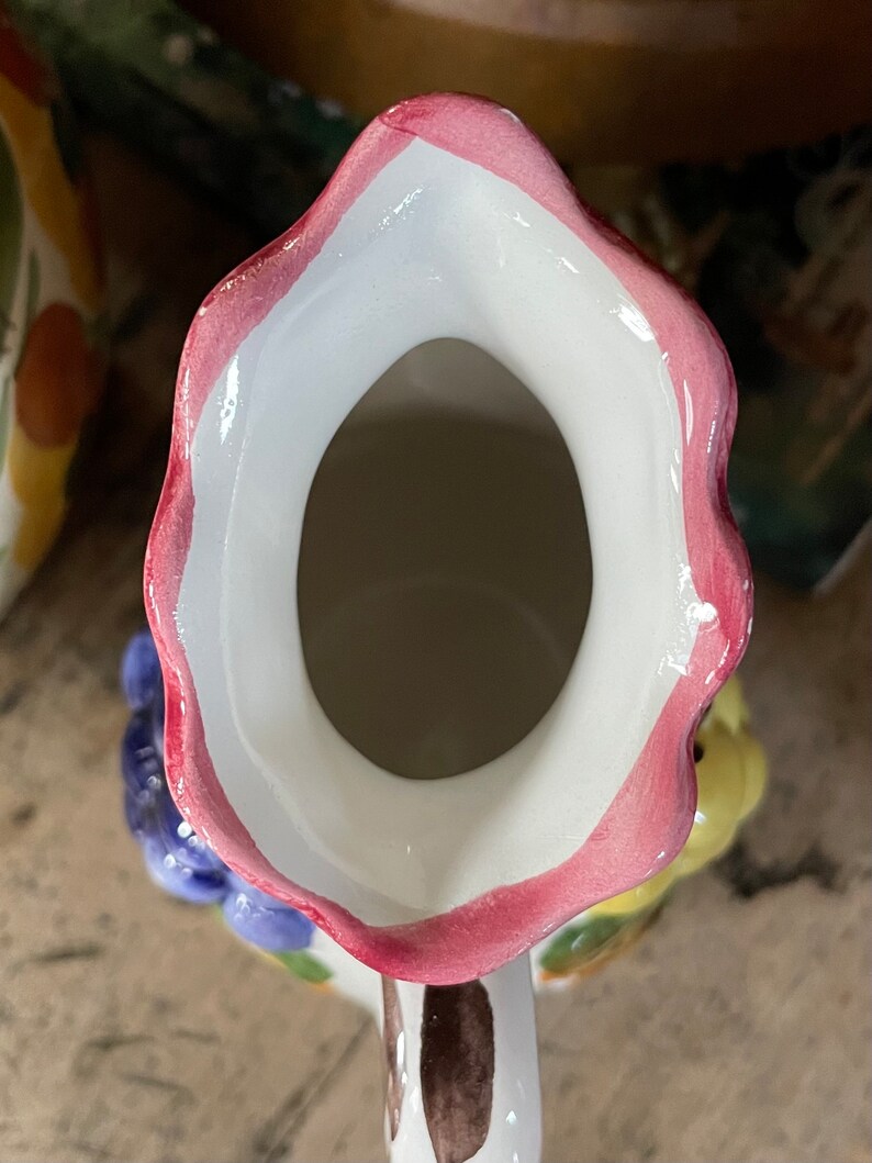 Puede incluir: Una jarra de cer&aacute;mica blanca con un borde rosa y un dise&ntilde;o floral. La jarra tiene una abertura ancha y un asa.