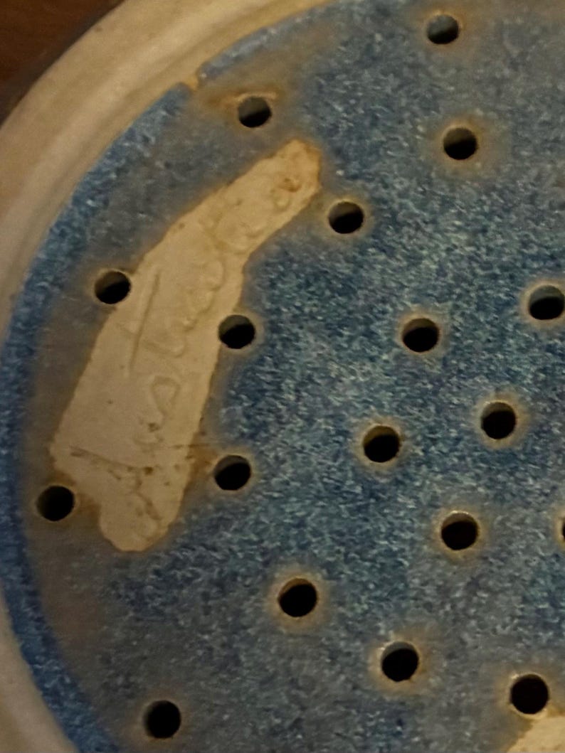 K&ouml;nnte beinhalten: Nahaufnahme einer Keramik-Gem&uuml;sesch&uuml;ssel mit blau gesprenkeltem Innenraum und zahlreichen kleinen L&ouml;chern. Ein Teil des Randes der Gem&uuml;sesch&uuml;ssel ist sichtbar, zusammen mit einem hellfarbigen, unregelm&auml;&szlig;igen Fleck mit verblasstem Text.