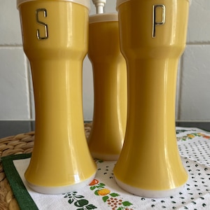May include: A set of three yellow ceramic salt and pepper shakers with white lids. The shakers have a gold 'S' and 'P' on the front.