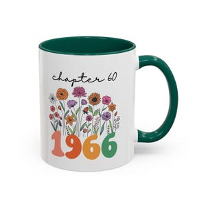 May include: White ceramic mug with a green handle and interior. The mug features the text "chapter 60" above a colorful floral design and the year "1966" in orange, yellow, and green.
