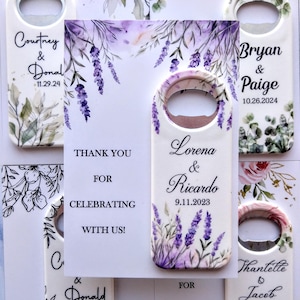 May include: Set of lavender-themed wedding bottle openers with a thank you card. The bottle openers feature a watercolor design with lavender flowers and greenery. The card says "Thank you for celebrating with us!" and has the names "Lorena & Ricardo" and the date "9.11.2023".