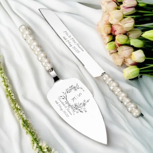 Könnte beinhalten: Ein silbernes Kuchenmesser- und -Server-Set mit perlmuttartigen Perlen an den Griffen. Das Messer hat die Gravur "Mr. & Mrs. Lawson 4th May 2023" auf der Klinge. Der Server hat ein florales Design mit den Initialen "S & K" und dem Text "Scarlett & Kieran 4th May 2023".
