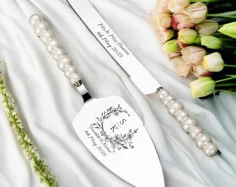 May include: A silver cake knife and server set with pearl-like beads on the handles. The knife has the text "Mr. & Mrs. Lawson 4th May 2023" engraved on the blade. The server has a floral design with the initials "S & K" and the text "Scarlett & Kieran 4th May 2023".
