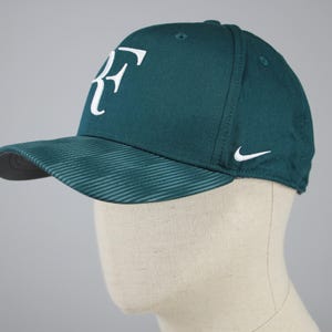 Può includere: Un cappello da baseball verde scuro con un logo "RF" bianco sul davanti e uno swoosh Nike bianco sul lato.