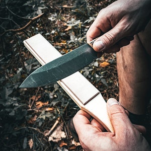 Puede incluir: Una persona afilando un cuchillo negro en un afilador de madera.