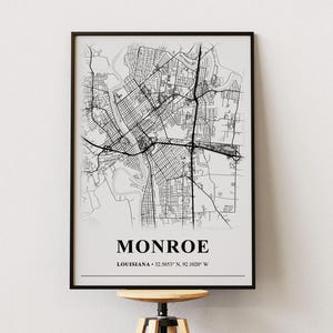 May include: A framed wall art print featuring a black and white street map of Monroe, Louisiana. The print includes the city name in bold capital letters, the state name, and the geographic coordinates 32.5053° N, 92.1020° W at the bottom.