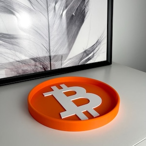 Pode incluir: Bandeja redonda laranja com um símbolo Bitcoin 3D branco em relevo no centro.