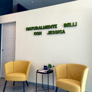 Pu&ograve; includere: Un'area d'attesa con due poltrone gialle e un tavolino nero. Sul muro la scritta "NATURALMENTE BELLI CON JESSICA" in lettere verdi. Il pavimento &egrave; piastrellato e il soffitto ha luci a incasso.