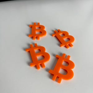 May include: Four orange plastic Bitcoin symbols on a white surface.