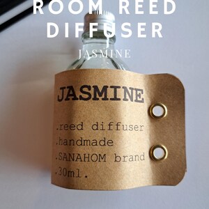 Könnte beinhalten: Eine klare Glasflasche mit einem braunen Papieretikett, auf dem "Jasmine" und "Rieddiffusor, handgefertigt, Marke SANAHOM, 30ml" steht.