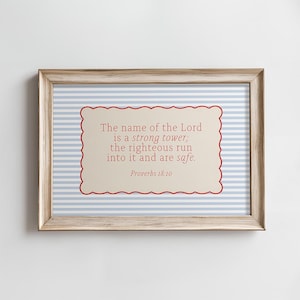 May include: Framed artwork with a light wood-tone frame. The background features blue and white stripes. The central focus is a cream-colored rectangle with a red scalloped border, displaying the text "The name of the Lord is a strong tower; the righteous run into it and are safe. Proverbs 18:10."