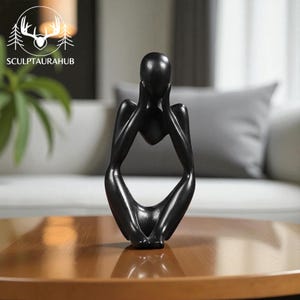 May include: A black sculpture of a person in a seated, contemplative pose. The figure's hands are placed on their face, with the head resting on the hands. The sculpture is on a brown table. The text "SCULPTAURAHUB" is in the background.